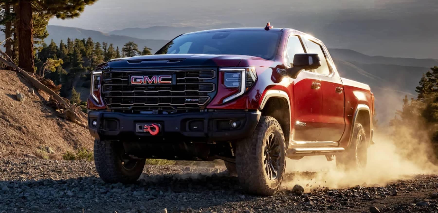 An exterior shot of a red GMC truck driving on a dirt road