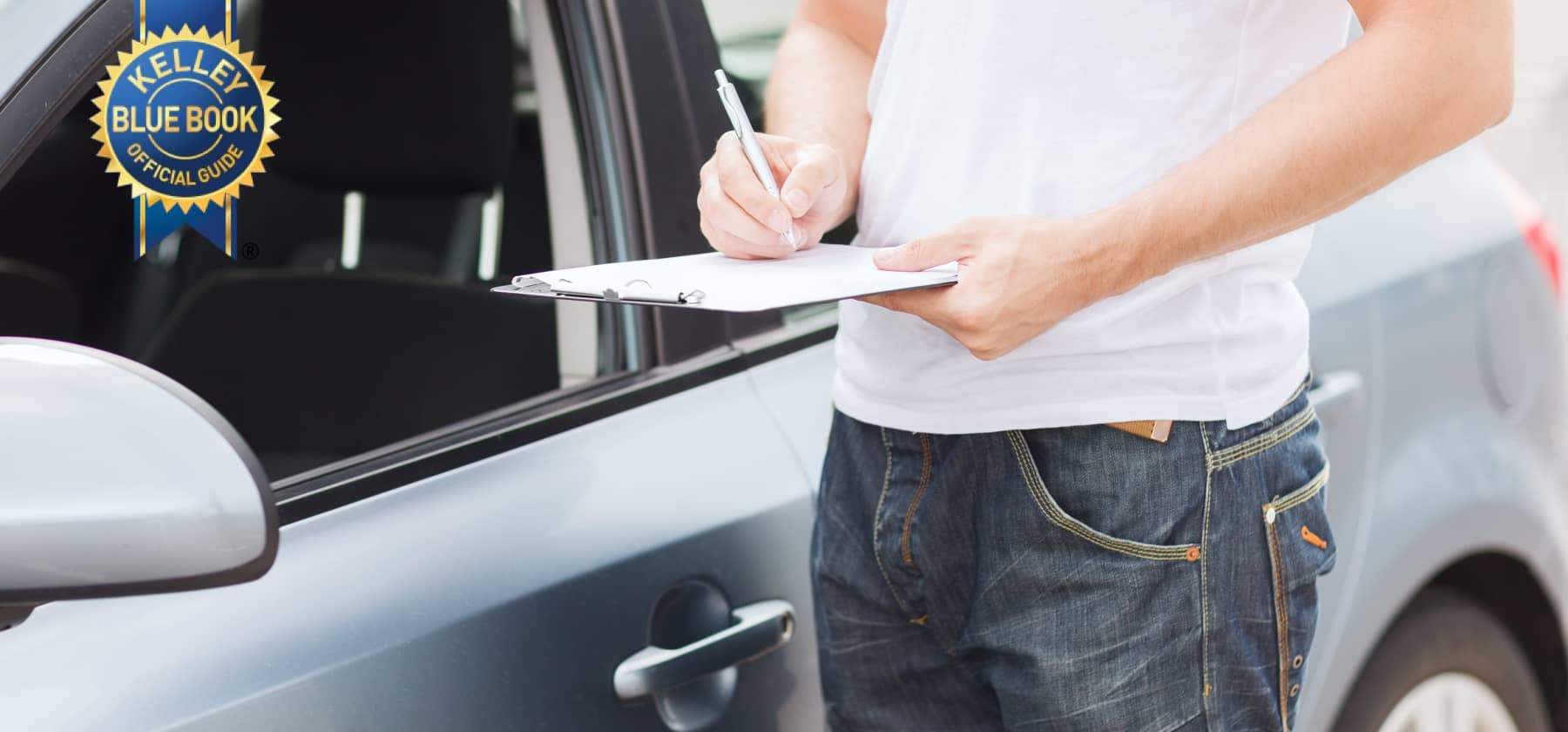 person filling out a clipboard next to car with Kelley Blue Book badge on it