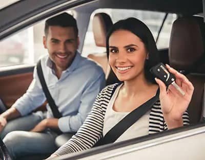 Woman and man sitting in car holding up new car keys