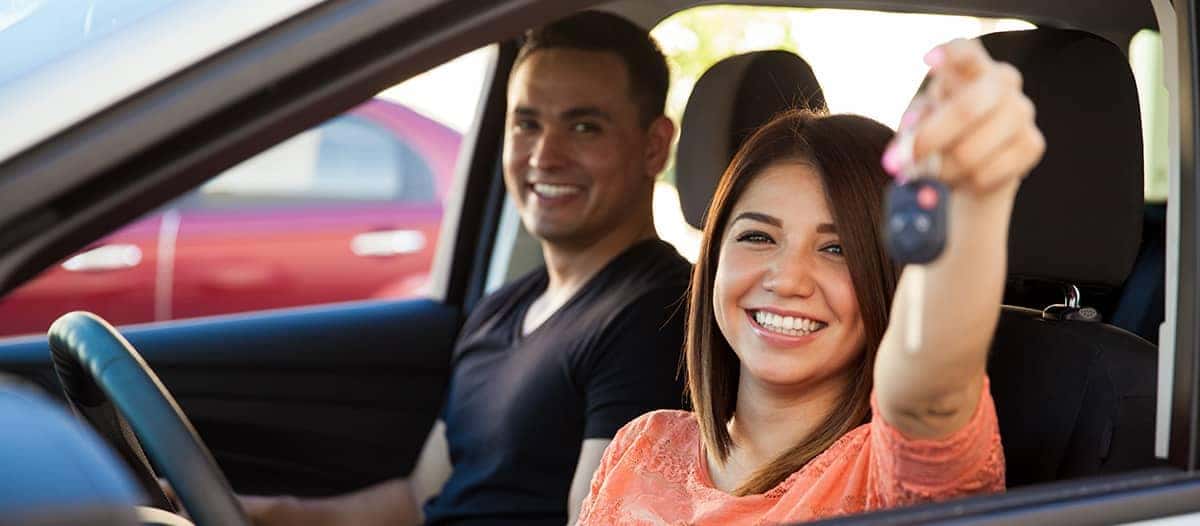 Woman holding keys out the drivers side window with a smile on her face
