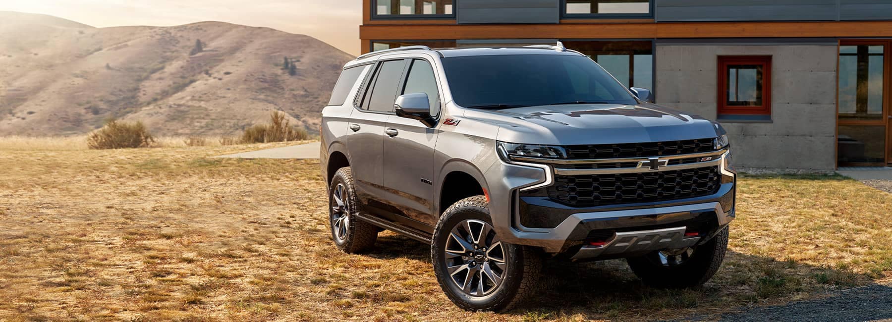 2022 Chevrolet Tahoe Z71 in Satin Steel Metallic Parked in Grass in Front of Mountains and a Home