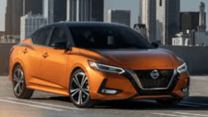 orange car with a black hard top with silver rims on a road with a city backdrop in the background.