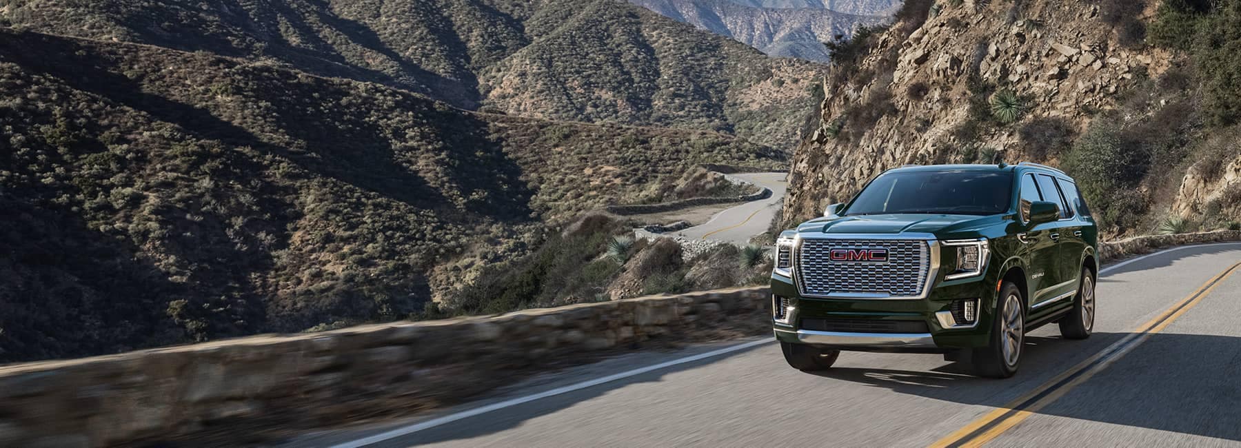 Front view of a green 2022 GMC Yukon Denali driving on a mountainside road