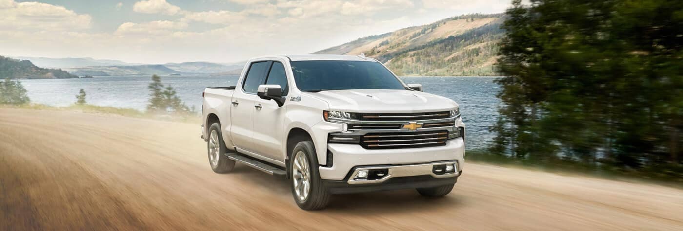 Front view of a white 2020 Chevy Silverado 1500 driving down a waterside dirt road