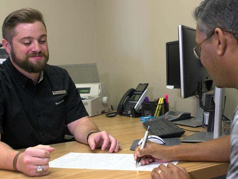 A happy customer is signing ownership papers with a staff member