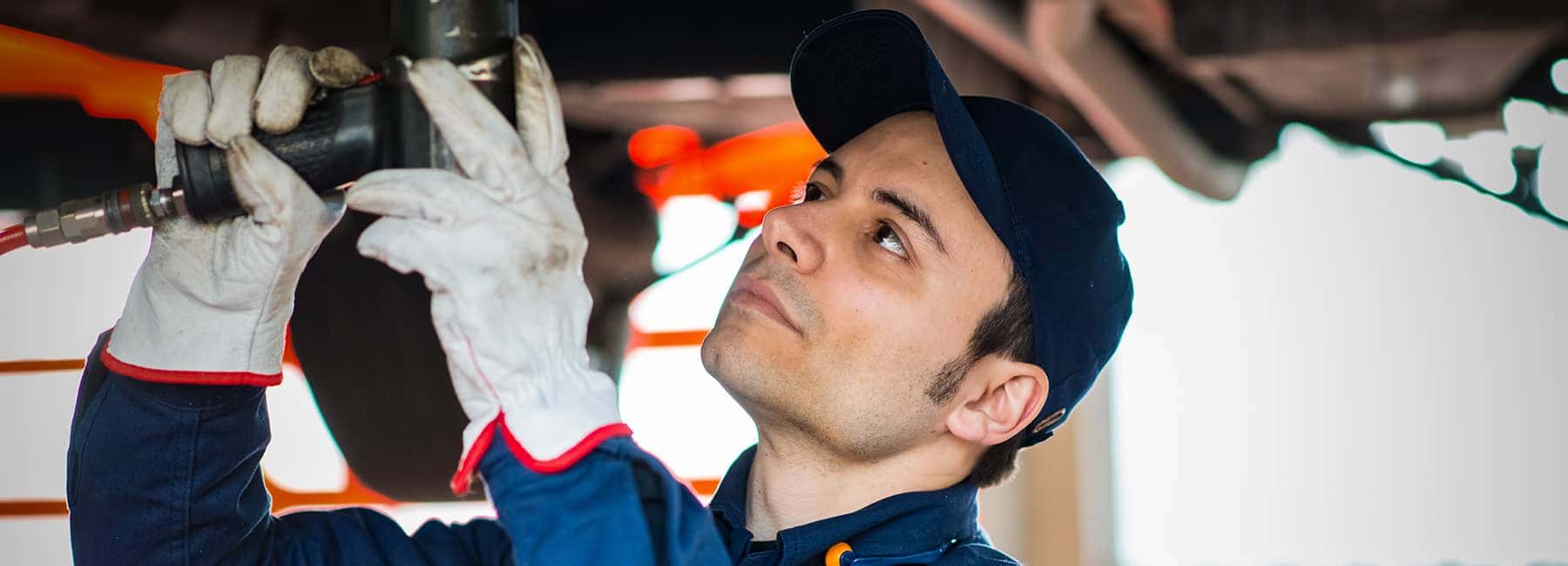 Service technician drilling the underside of a car
