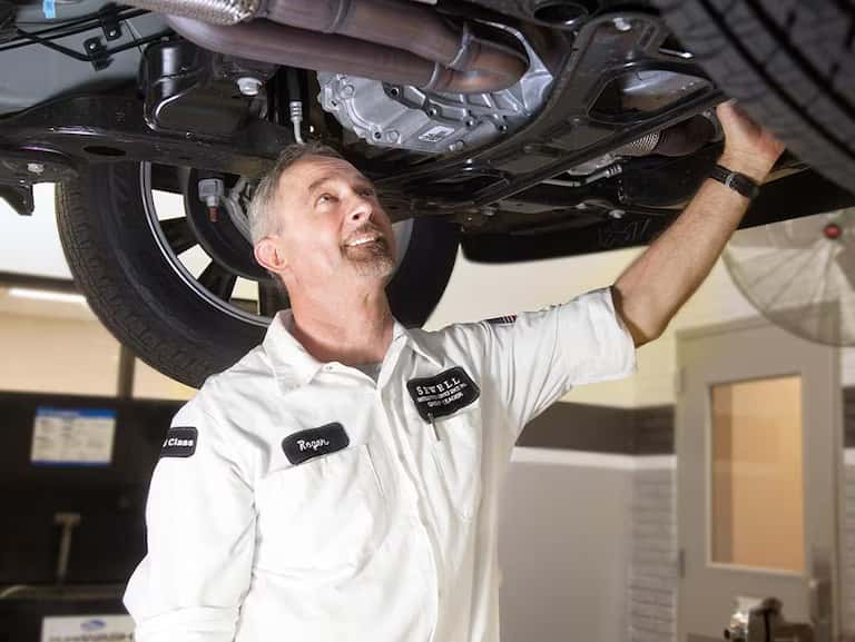 Sewell service technician looking at the bottom of a raised car
