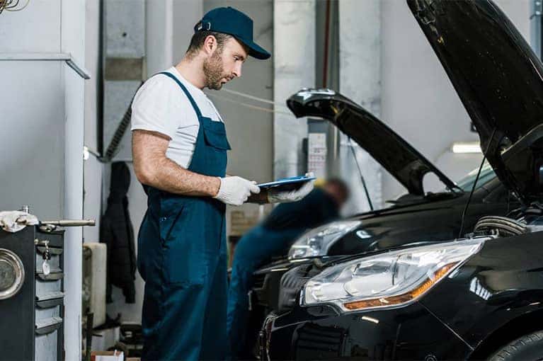 Mechanic reviews a service order in front of a car engine