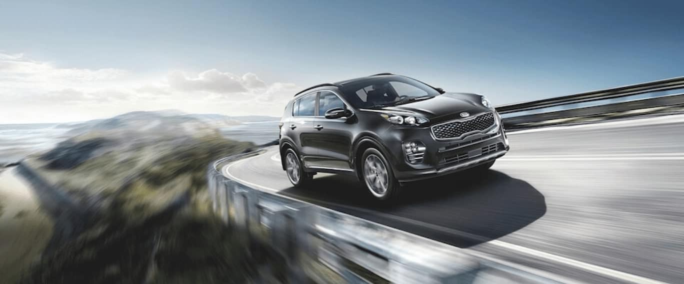 A black 2019 kia Sportage driving around a curve on an open highway
