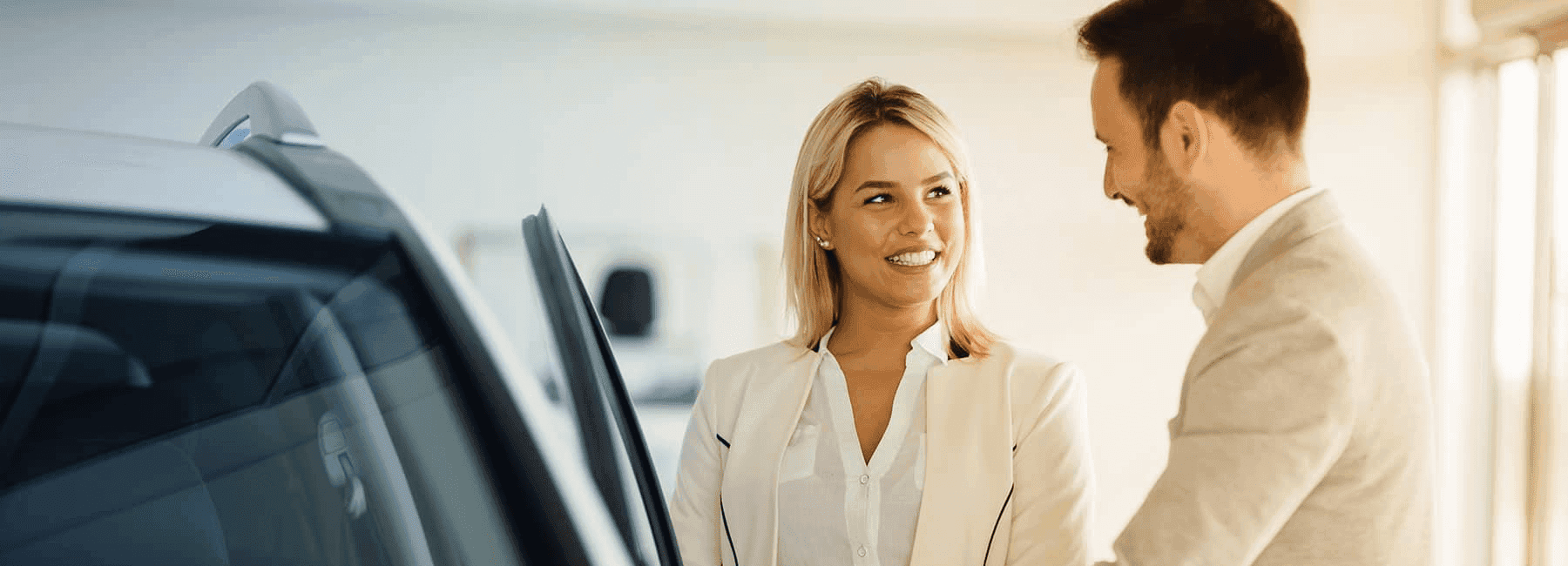 car salesman shows happy woman car in showroom