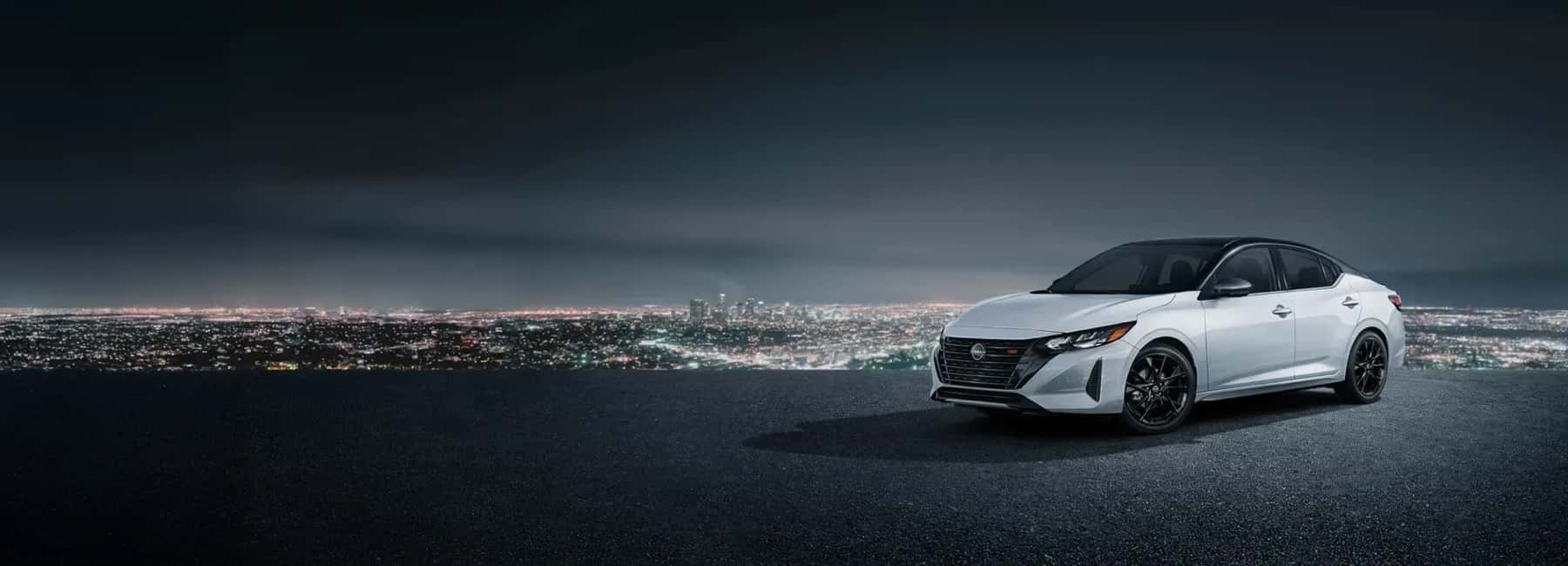 white Nissan sedan parked overlooking city at night