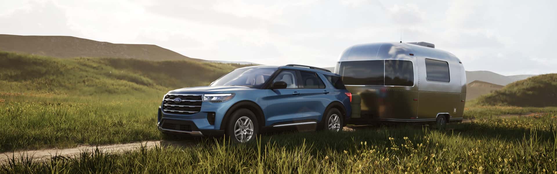 2026 Ford Explorer in Vapor Blue Metallic pulling a camper over a dirt road to a campsite