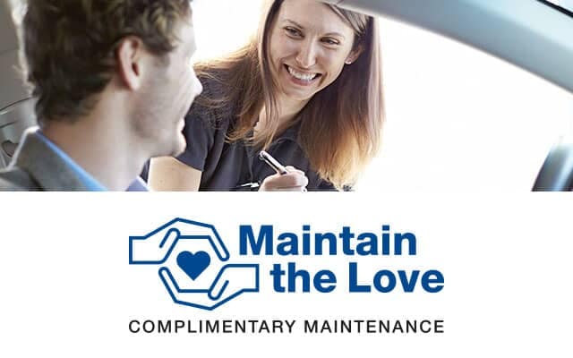 woman sales rep speaking to a Subaru driver in their car with maintain the love logo at the bottom of the image