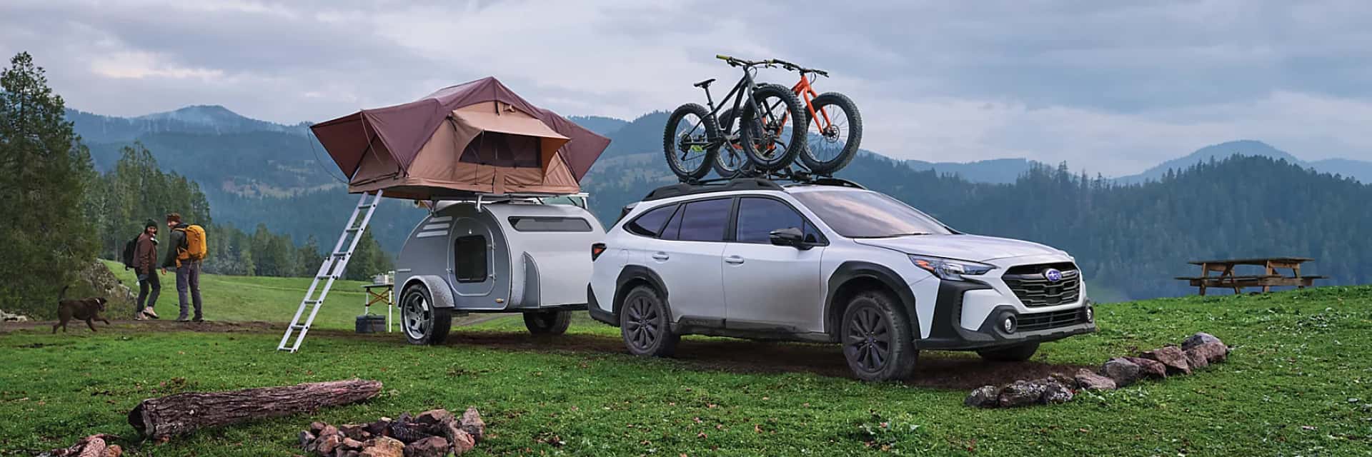 2024-Subaru-Outback-with-a-trailer-attached-and-two-bicycles-on-top-while-parked-near-a-forest
