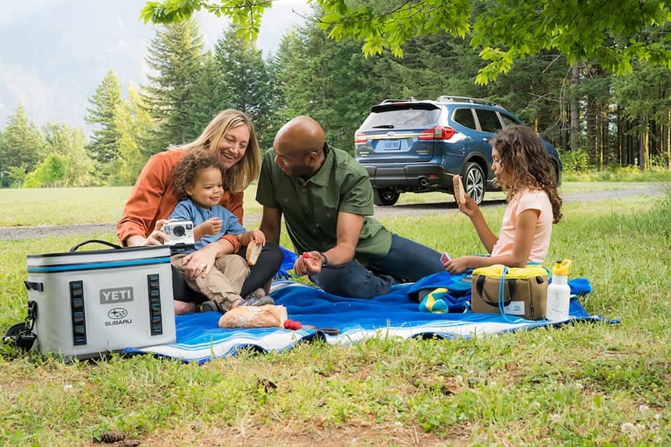 Family having a picnic with Subaru parked behind them