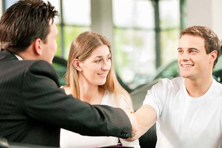 happy couple shaking car salesman's hand
