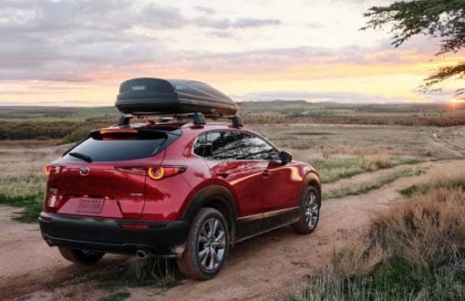 A red Mazda hatchback is parked on a desert trail.