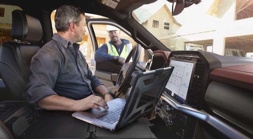 A person is shown using a laptop in a 2023 Ford F-150 at a construction site.
