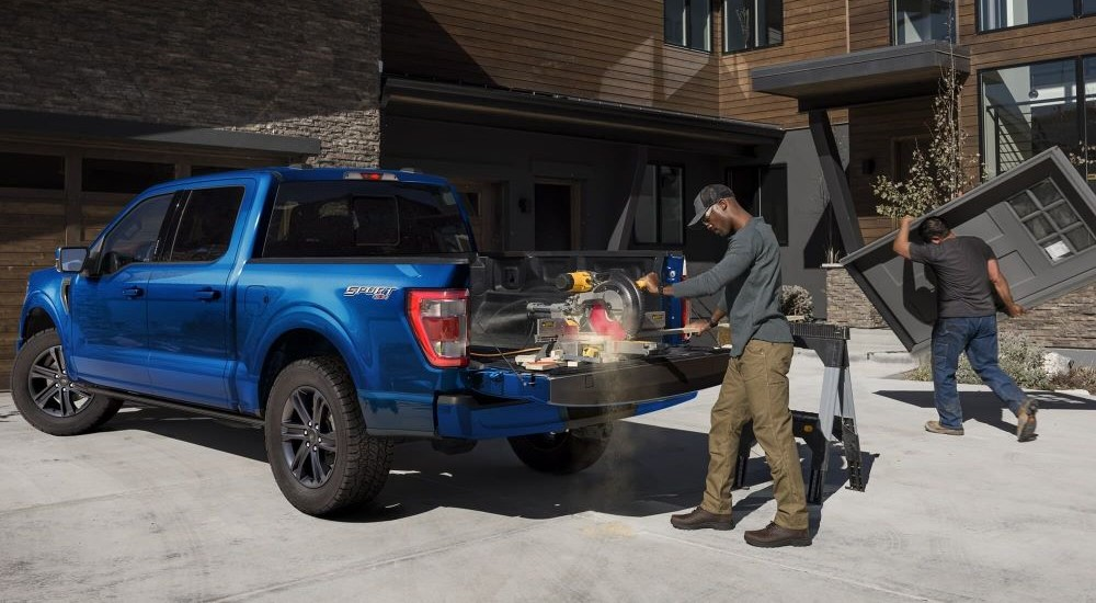 A person is shown using a chop saw on the bed of a blue 2023 Ford F-150 Sport.