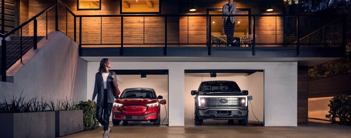 A red 2023 Ford Mustang Mach-E a silver F-150 Lightning are shown charging in a garage.