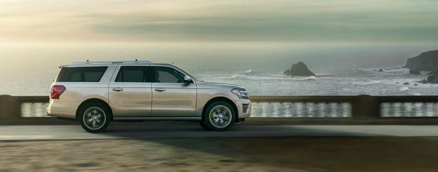A silver 2023 Ford Expedition is shown from the side driving past an ocean.