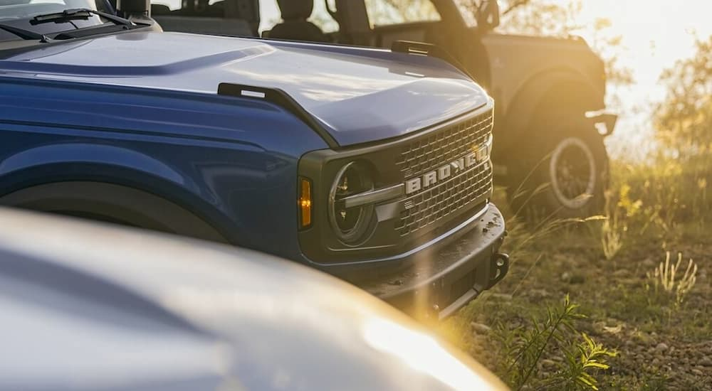 The front of a blue 2023 Ford Bronco is shown parked between two vehicles in a grassy area after leaving a Ford dealer.