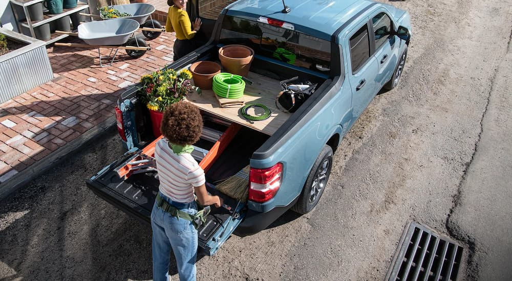 A woman is shown putting gardening supplies into the bed of a blue 2023 Ford Maverick.