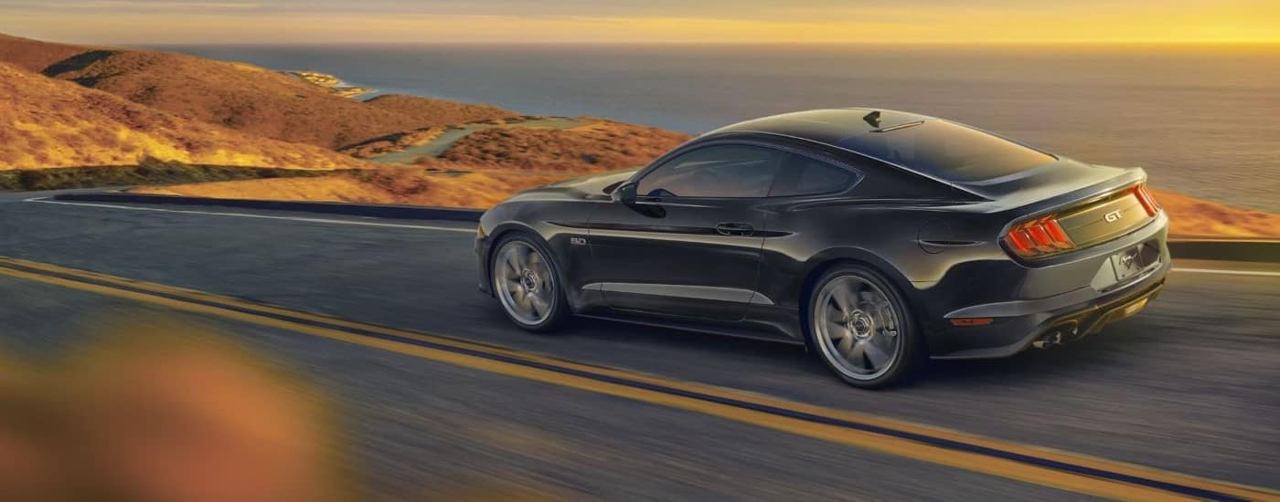 A black 2022 Ford Mustang GT is shown driving on a coastal road.