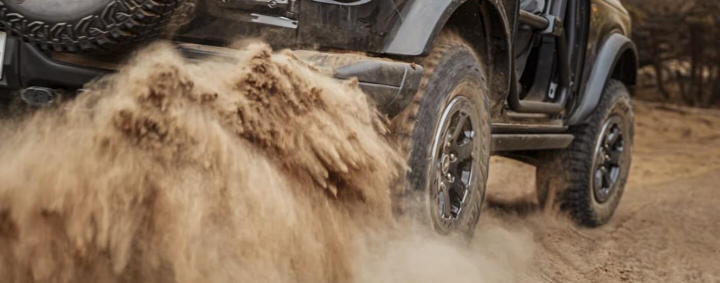 A black 2022 Ford Bronco is shown kicking up dust after leaving a Ford dealer.