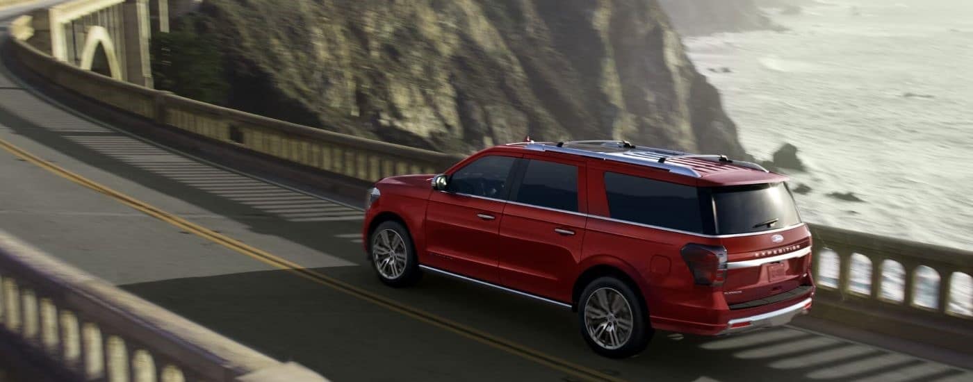 A red 2023 Ford Expedition is shown driving on a bridge near the ocean.