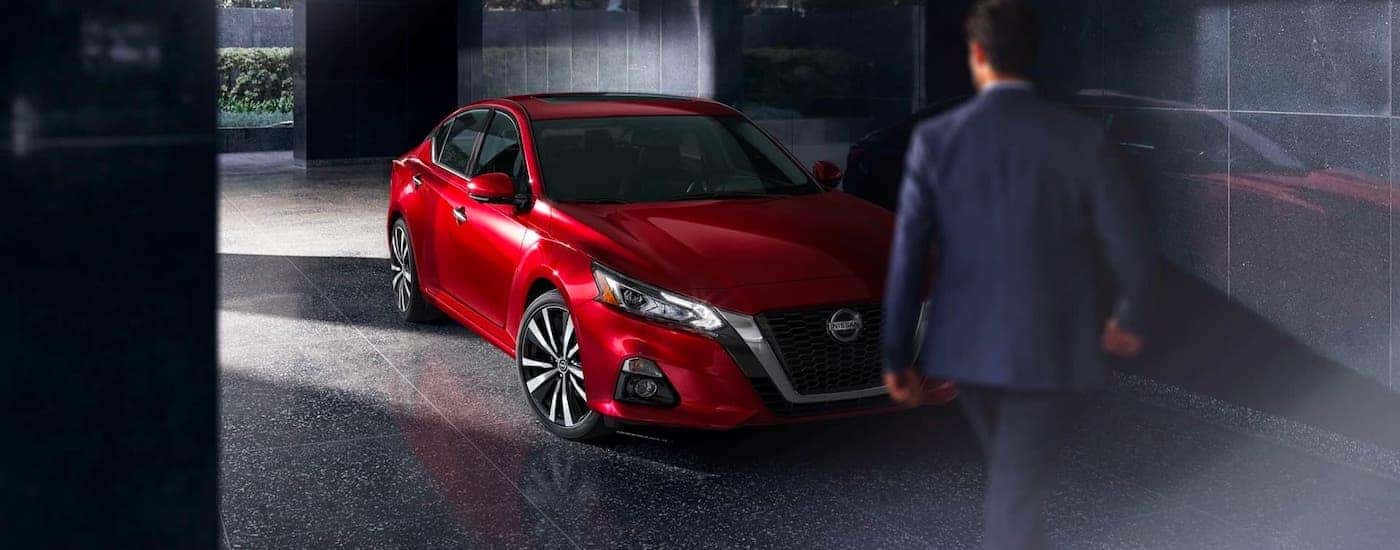 A man is walking towards a red 2020 Nissan Altima which is parked in a stone corridor.