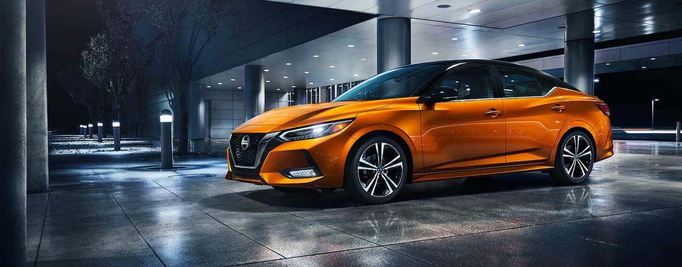 An orange 2020 Nissan Sentra is parked outside a local Nissan dealer at night.