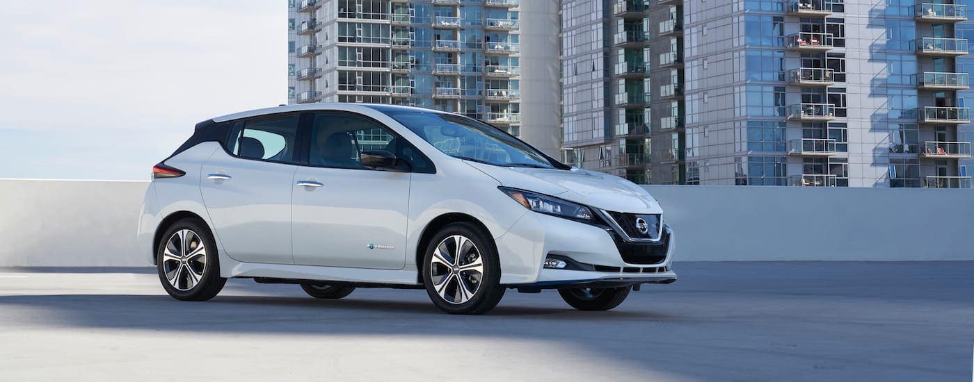 A white 2020 Nissan Leaf is parked on a parking garage in front of a large apartment building.