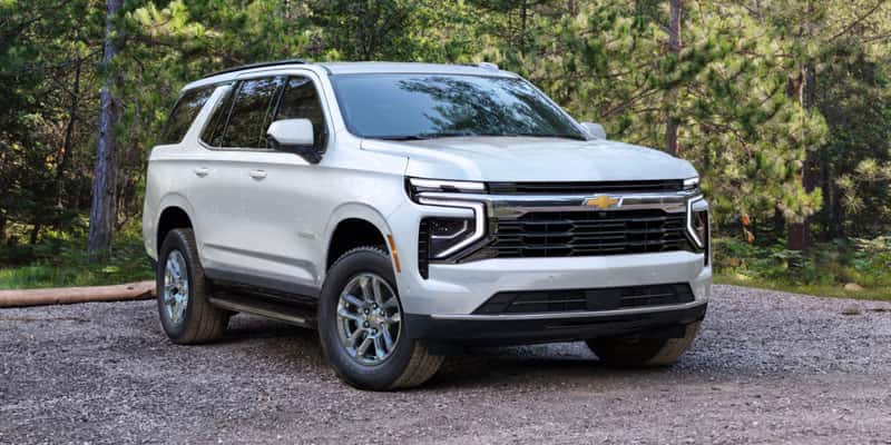 An all-new white 2025 Chevrolet Tahoe parked in a gravel lot in the woods. - Toliver Brothers Ballinger, TX