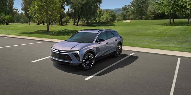 An all-new silver 2025 Chevy Blazer EV in a parking lot in front of a city park. - Toliver Brothers GM Ballinger, TX