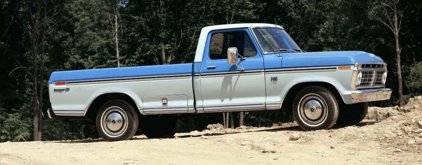 A red 1948 Ford F-1 is parked on a dirt path near a wooded hill.