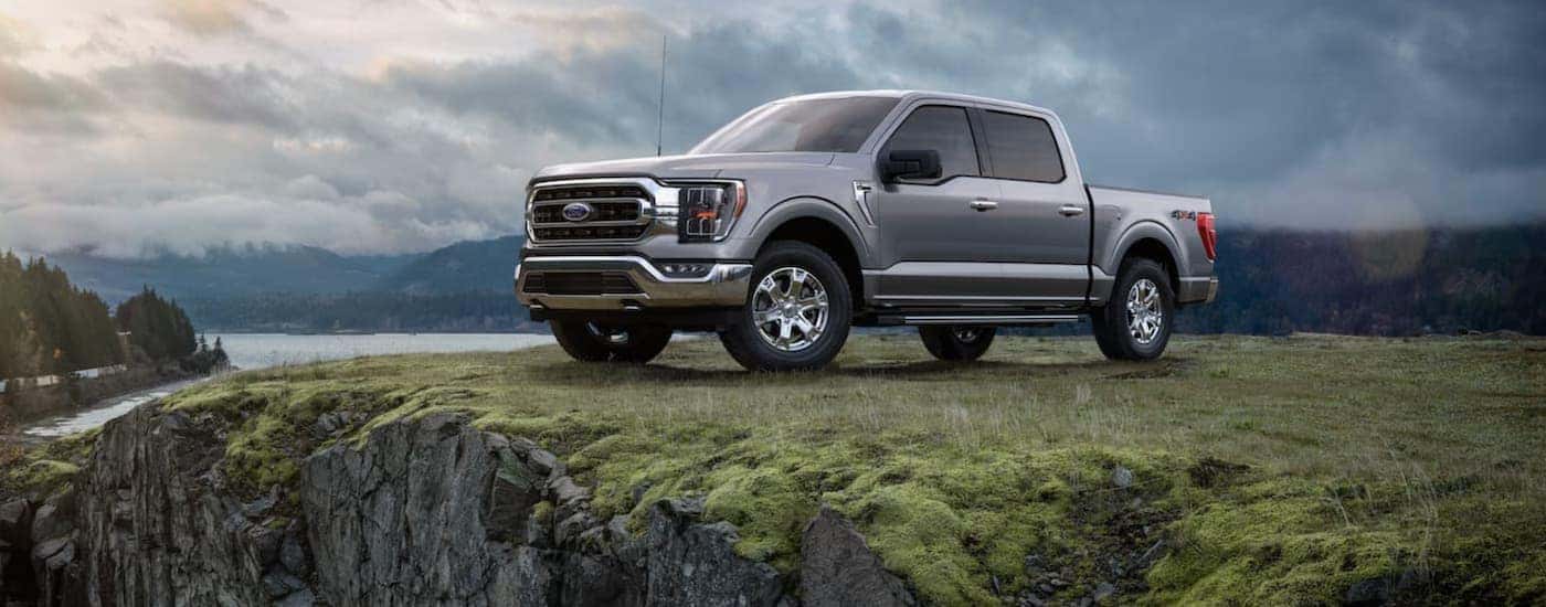 A popular vehicle at your used Ford truck dealership, a silver 2021 Ford F-150, is shown parked on the grass next to a lake.