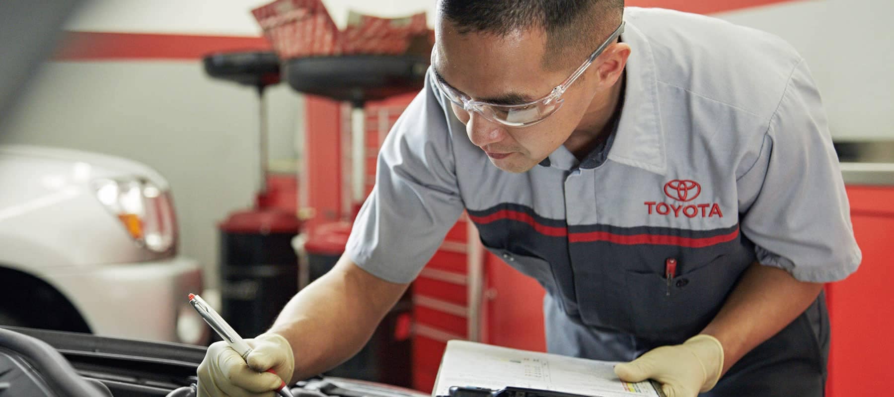 Toyota service technician holding a clipboard and inspecting a car engine