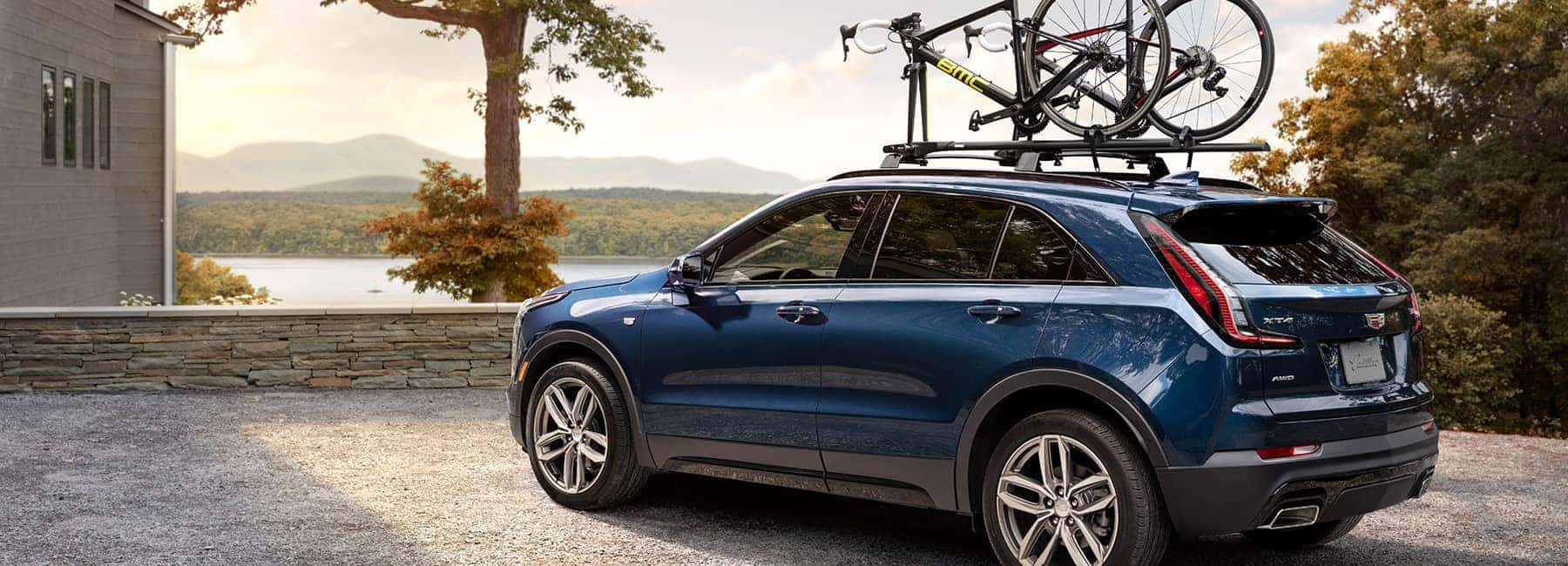 Cadillac Banner Image - A royal Blue Cadillac SUV/Crossover with a bike on the roof rack parked at a lake