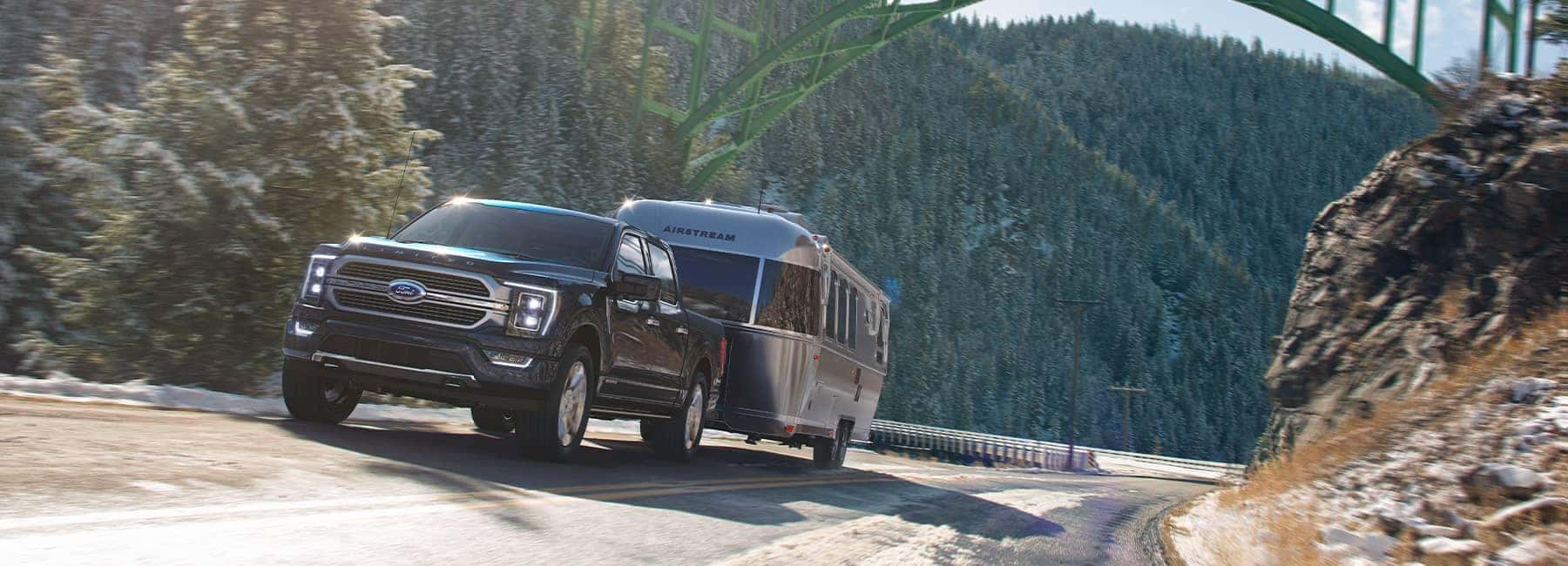 A black Ford F150 hauling a silver Airstream RV through a mountain pass