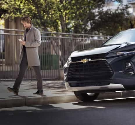 Man looking at his phone while walking past a parked Chevrolet
