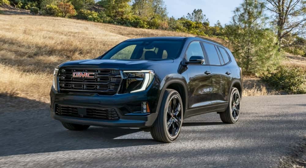 Black 2025 GMC Acadia Elevation driving on a country road