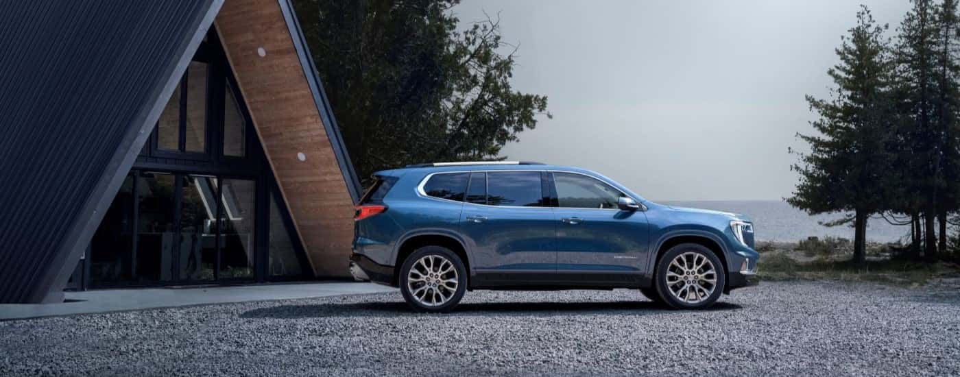 Blue 2024 GMC Acadia Denali parked in front of a cabin