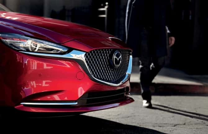 A man is walking toward a parked red Mazda