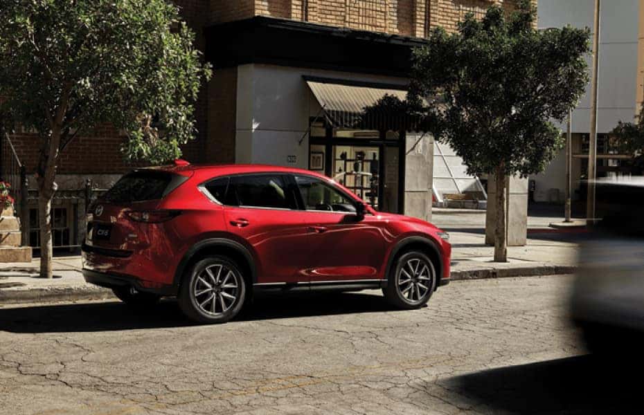 A red Mazda hatchback is parked on the side of a city sidewalk