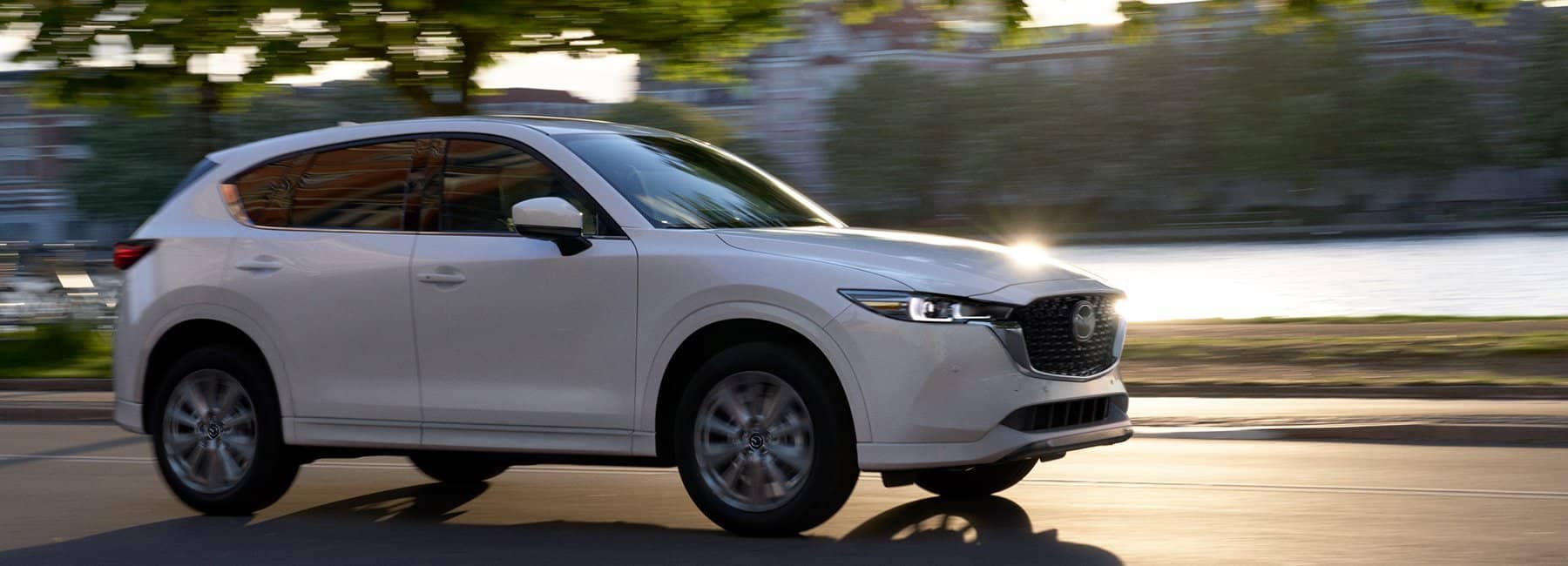 2022-mazda-cx-5-compact-suv-sideview-driving-blurred-trees-lake-white