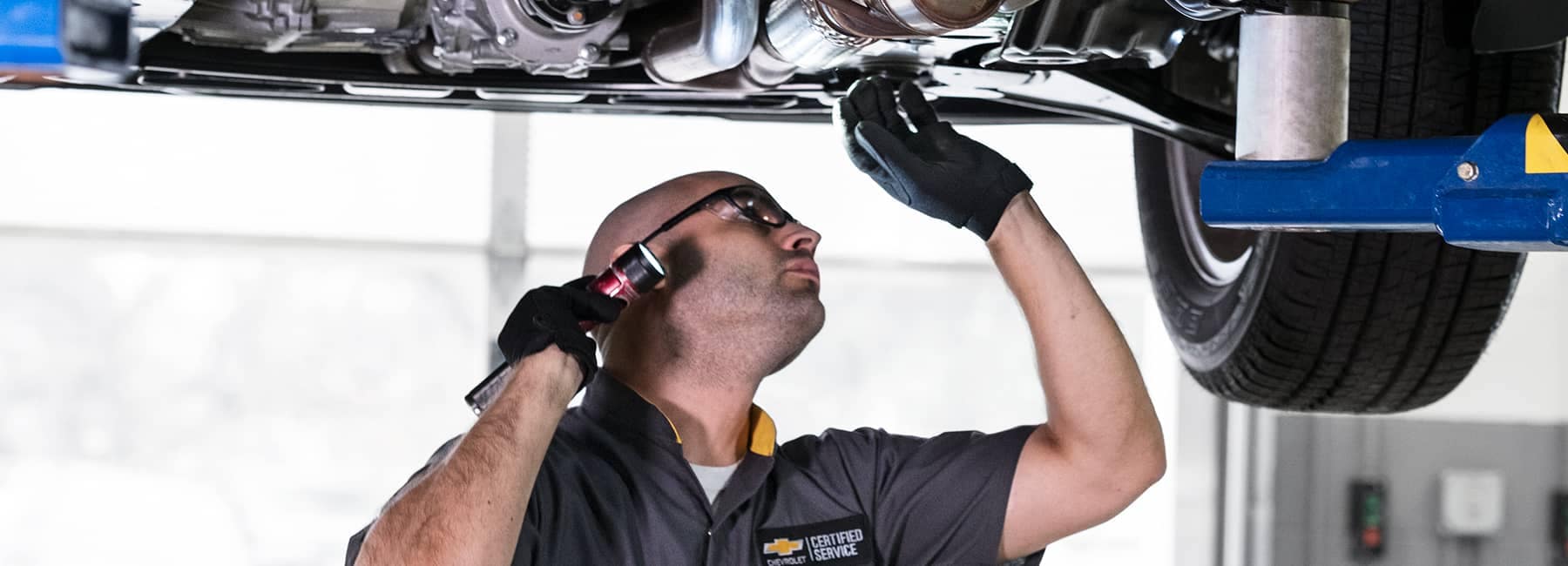Chevrolet service technician looking at underside of a raised car
