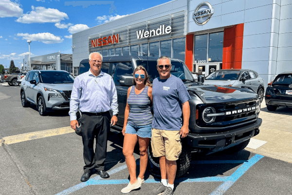 A group of people standing in front of a car