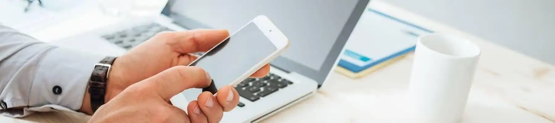 Hands are holding a mobile device next to a laptop
