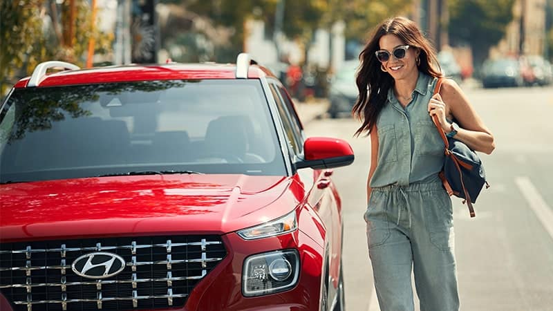 red Hyundai parked on road with smiling woman
